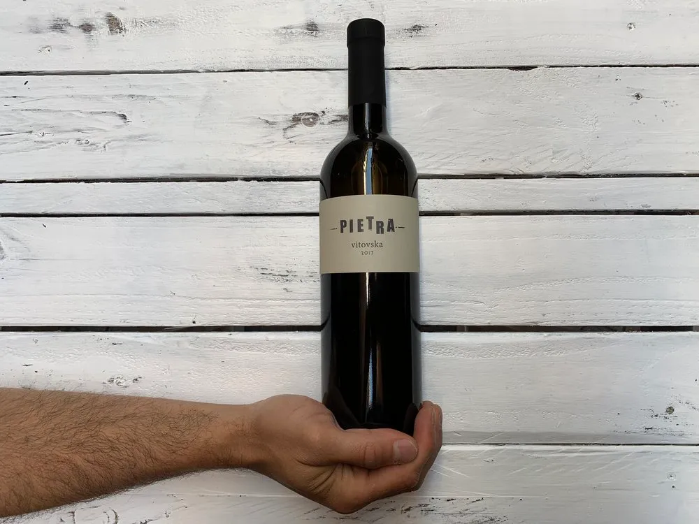 Bottiglia di vino naturale in mano su legno bianco